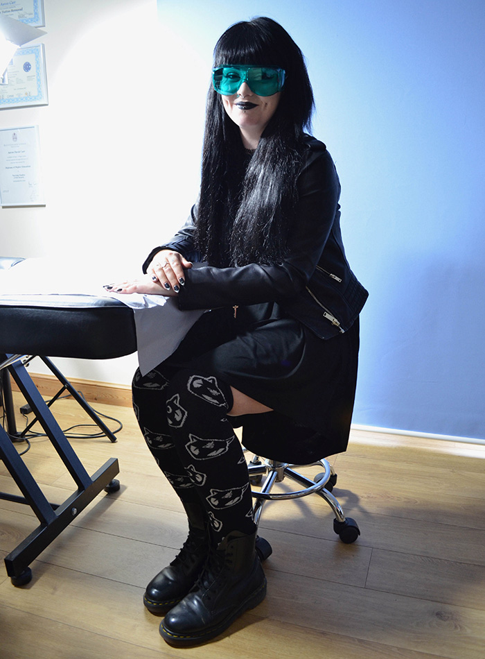 Goth beauty with long black hair and green laser goggles smiling after treatment